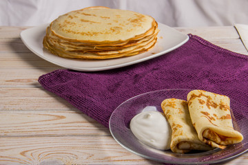 Two pancakes on a plate with sour cream on a light background and a lilac towel