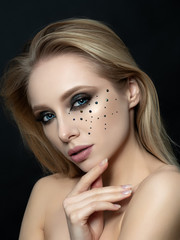 Fototapeta premium Close up beauty portrait of young woman with beautiful fashion makeup touching her face. Modern fashion makeup. Long lashes, bronze smokey eyes, black rhinestones. Studio shot.