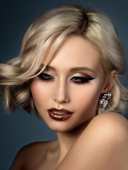 Fototapeta premium Portrait of young beautiful woman with evening make up. Modern fashion eyeliner wing and glitter on her lips. Studio shot.