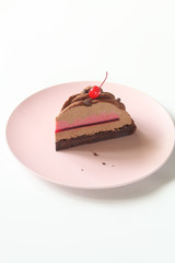 Slice of Contemporary Chocolate Cherry Mousse Cake covered with velvet spray, on a pink plate, on white background. 