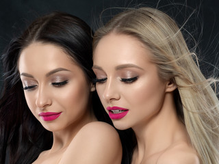 Closeup portrait of two young beautiful women over black background. Bright pink lipstick. Skin care, cosmetics, SPA therapy or cosmetology concept