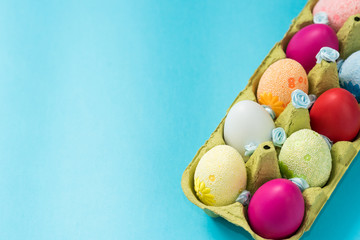 Easter eggs are painted in bright colors, lie in a cardboard eco-packaging. Blue background. Easter ideas. Space for text. Egg eco tray. Happy easter.