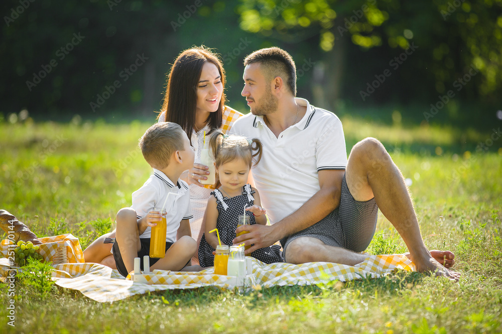 Wall mural Young family having picnic outdoor. Mother, father and their kids having fun in the park. Summer resting at the nature.