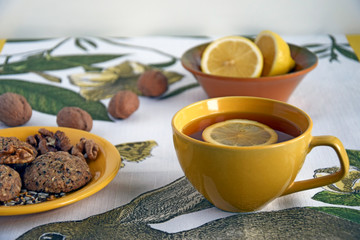 A cup of green tea with lemon, biscuits with walnuts, flax and sesame seeds, sliced lemon, whole walnuts. The concept of healthy eating.