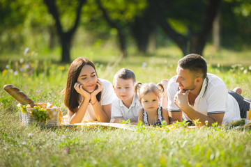 Fototapeta premium Young family having picnic outdoor. Mother, father and their kids having fun in the park. Summer resting at the nature.