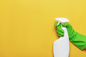 A worker's hand in a rubber protective glove with a spray bottle on a yellow colored background....