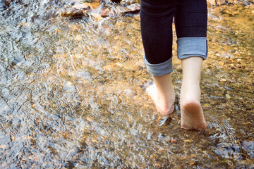 beautiful lady that wear jeans is walking on the stones in river.