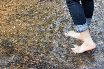 beautiful lady that wear jeans is walking on the stones in river.