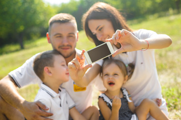 Cheerful young family making selfie at the picnic outdoor. Beautiful family together having fun. Day off with children. Young parents with their kids making mobile picture.