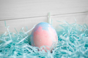 Colorful Easter egg painted by hand in straw nest on white wooden rustic background.