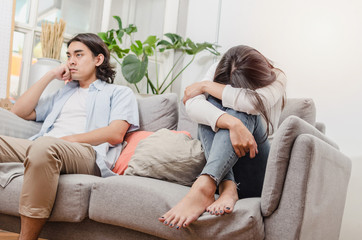 sadness young asian wife having quarrel and sitting on sofa after fight with husband behind her in...