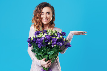 Young happy smiling redhead woman holding bouquet of violet spring flowers isolated on blue background. Festive bouquet in honor of women's day on March 8 or birthday