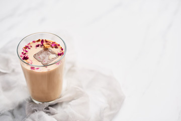 Iced coffee with rose and cardamom in a tall glass on white and gray silk background. Copy space...