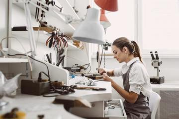 Busy working. Side view of young female jeweler working on a new jewelry product at her workbench....