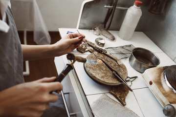 Delicate work. Side view of jeweler's hands soldering a silver earring with flame from welding torch