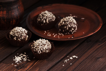 Close-up chocolate pralines with coconut on a dark rustic wooden table. Homemade sweets.. Selective focus