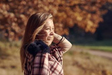 Young beautiful girl with the long blond hair is standing on the autumn park against colorful tree. The wind is waving her hair.