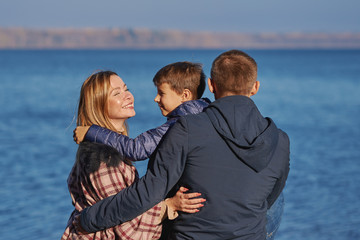 Young beautiful woman and her family are sitting near the picturesque lake. They are enjoying their trip and the atmosphere around.