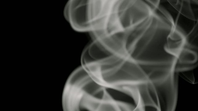 Thin trickle of white smoke slowly rising graceful twists up on black background. Black and white smoke blowing from bottom to top. Closeup