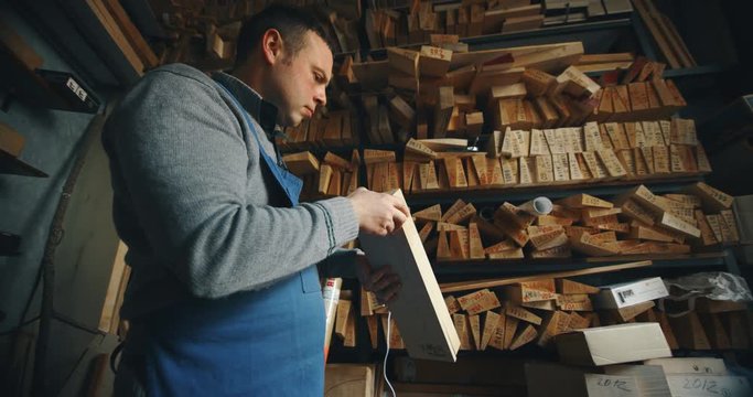  Slow motion of master artisan luthier choosing a wood for creation of handmade violin  in a workshop.