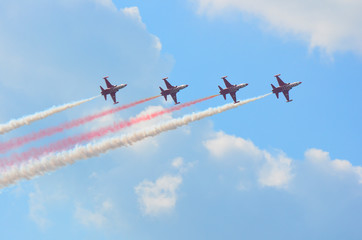 Formation of four stunt jets flying on a cloudy blue sky leaving red and white smoke trails - Image