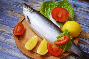Delicious herring with lemon and tomatoes on lettuce leaves.