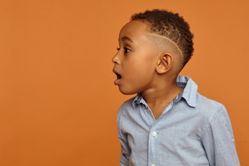 Obraz premium Wow. Amazed astonished handsome Afro American child with stylish hairdo posing isolated at blank copyspace studio wall, opening mouth widely, expressing great surprise and fascination, jaw dropped