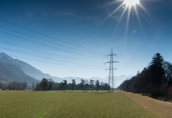 high voltage power lines and tall lattice crosses in rural countryside with snow-capped mountain peaks in the background