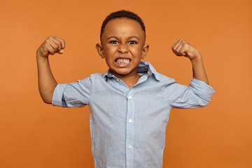 Fierce angry emotional dark skinned male expressing fury or rage keeping fists and teeth clenched, being mad with bully, ready to punch him back. Negative human facial expressions and reaction
