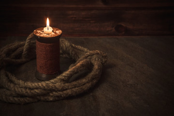 Fototapeta na wymiar old candle and rope on pirates table, place for text, real flame, stone and wood