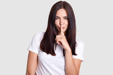 Girl like sly poses in photography. This photo is isolated. Background gray tint where model is in center. Lady wears white t shirt that fits impeccably to manicure on her finger near mouth.