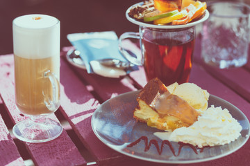 Outdoor cafe. Wooden vintage table and coffee, tea and cake on it. Shallow depth of field and a matte filter in an intagram style.