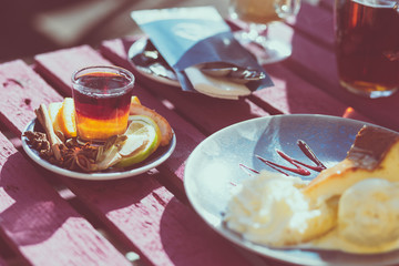 Outdoor cafe. Wooden vintage table and coffee, tea and cake on it. Shallow depth of field and a matte filter in an intagram style.