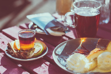 Outdoor cafe. Wooden vintage table and coffee, tea and cake on it. Shallow depth of field and a matte filter in an intagram style.