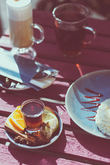Outdoor cafe. Wooden vintage table and coffee, tea and cake on it. Shallow depth of field and a matte filter in an intagram style.
