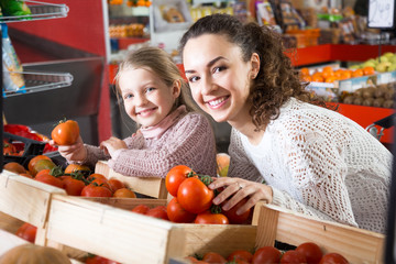 portret of young woman with beautiful daughter choosing tomatoes at store