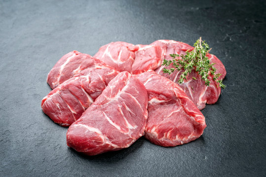 Traditionelle rohe Schweinebäckchen mit Kräuter als closeup auf einem schwarzen Board