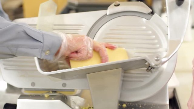 Close-up of a saleswoman slicing cheese in a supermarket and wrapping it in cling film. Packaging of chopped cheese in a supermarket worker.