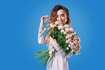 Portrait of happy brunet young woman with bouquet of pink spring flowers over blue background. Festive bouquet in honor of women's day on March 8 or birthday