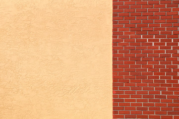 A blank empty yellow stucco wall joins to a red brick wall, outside.