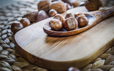 Shelled whole hazelnuts on a wooden spoon over a cheese board with mixed nuts in background