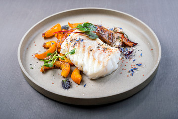 Fried Danish skrei cod fish filet with pumpkin, mushroom and lettuce as closeup on a modern design...