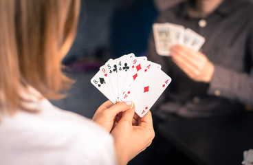 Friends are playing cards together at home. Woman is holding cards in her hands, man in the blurry background.