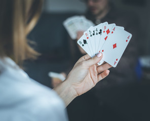 Friends are playing cards together at home. Woman is holding cards in her hands, man in the blurry background.