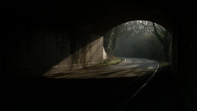 Railway underpass with road in shadow under a late afternoon sky.