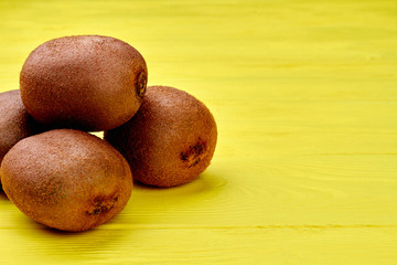 Heap of whole healthy kiwi and copy space. Kiwi fruits on yellow wooden table and text space. Healthy organic food.