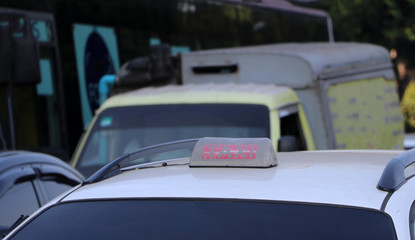 Taxi light sign or cab sign in drab white and red color with white text on the car roof.
