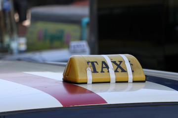 Taxi light sign or cab sign in yellow color with black text and tied with tape on the car roof.