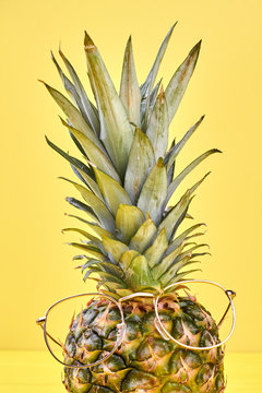 Green exotic pineapple on yellow background. Fresh natural ananas with green crown wearing eyeglasses on color backgorund, vertical image.