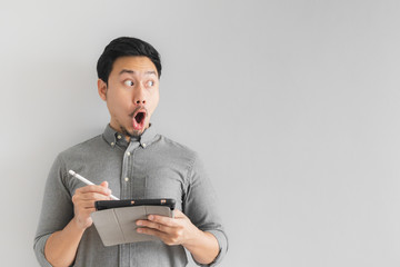 Wow and surprised entrepreneur businessman work on his tablet with grey background.